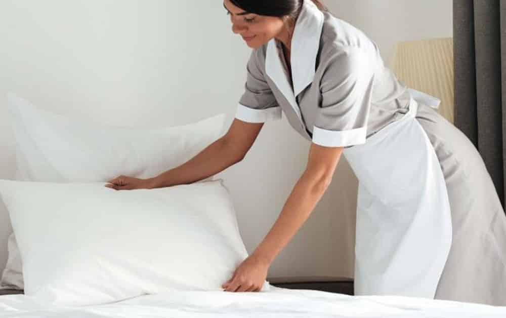 Rengøringsvikar der hjælper med at gøre en i seng i et hotelværelse rent