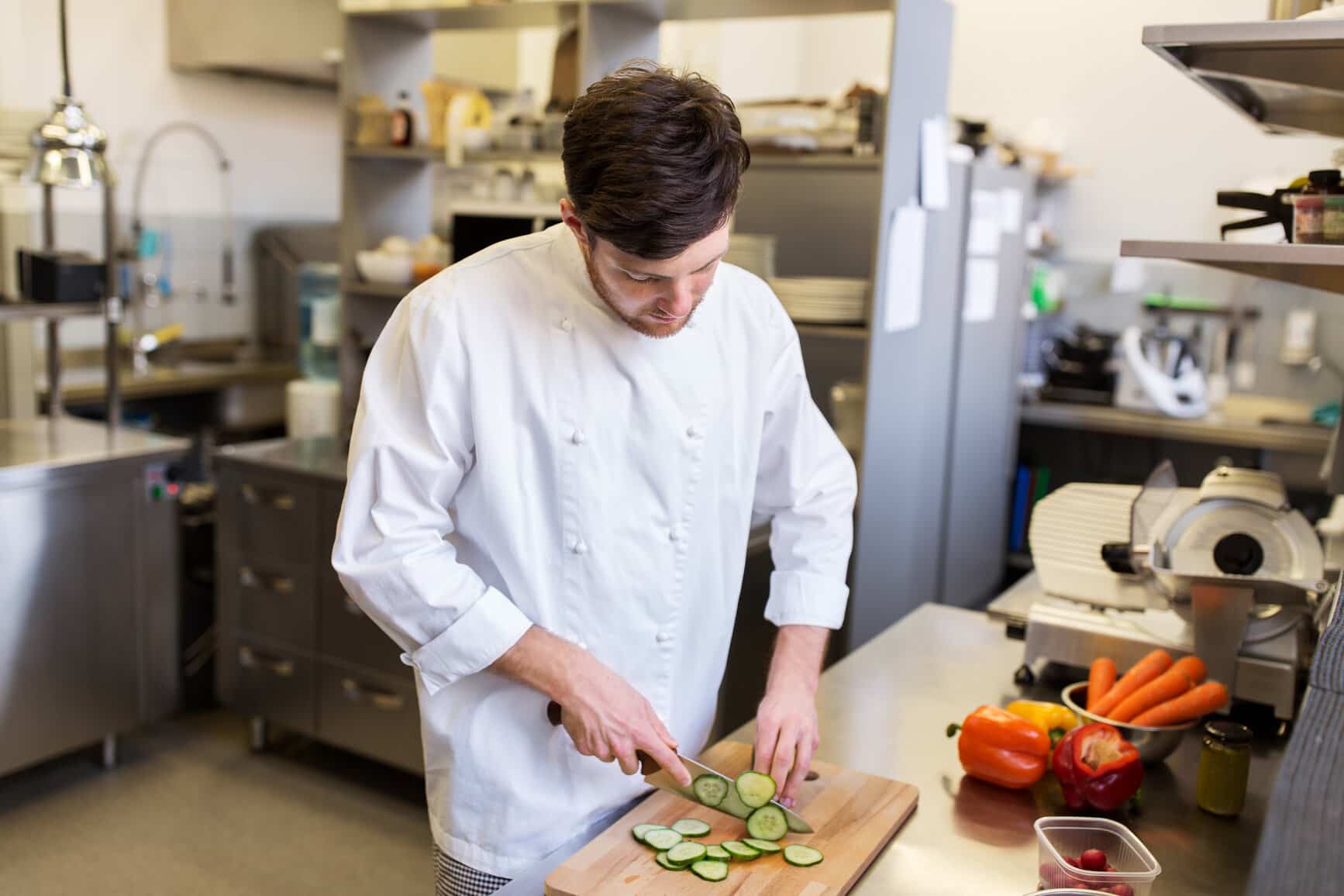 En mandelig køkkenmedhjælper, der skærer grønt i et køkken.