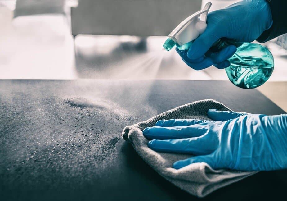 En person med blå håndsker rengør et bord med en sprayflaske.
