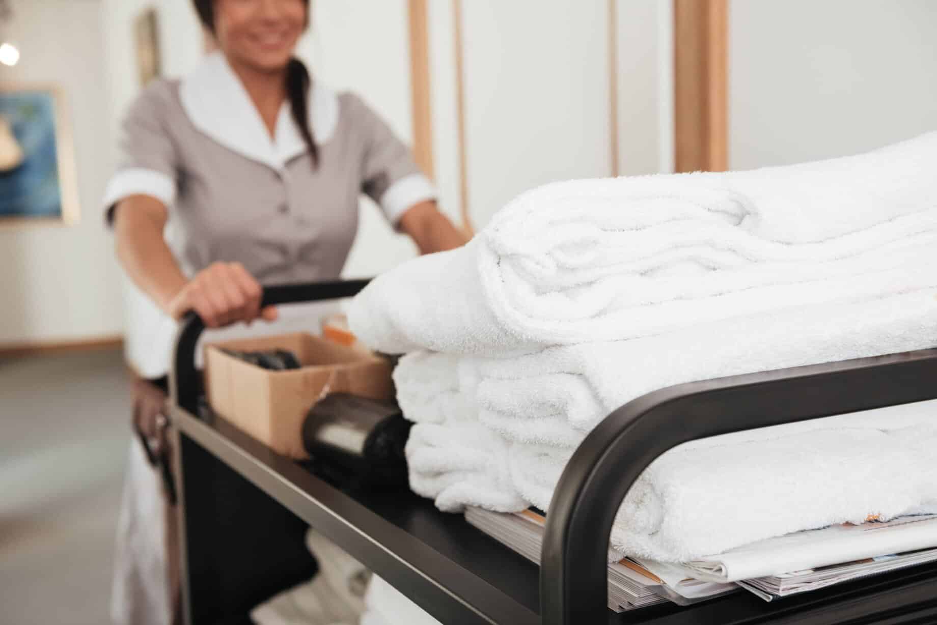 En stuepige med en vogn fuld af håndklæder på et hotelværelse.